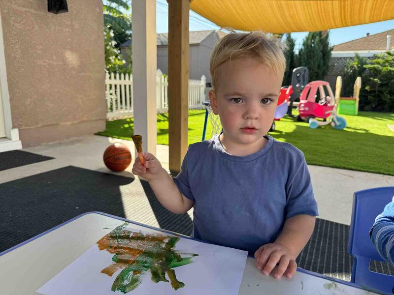 Child painting outdoors with yard visible